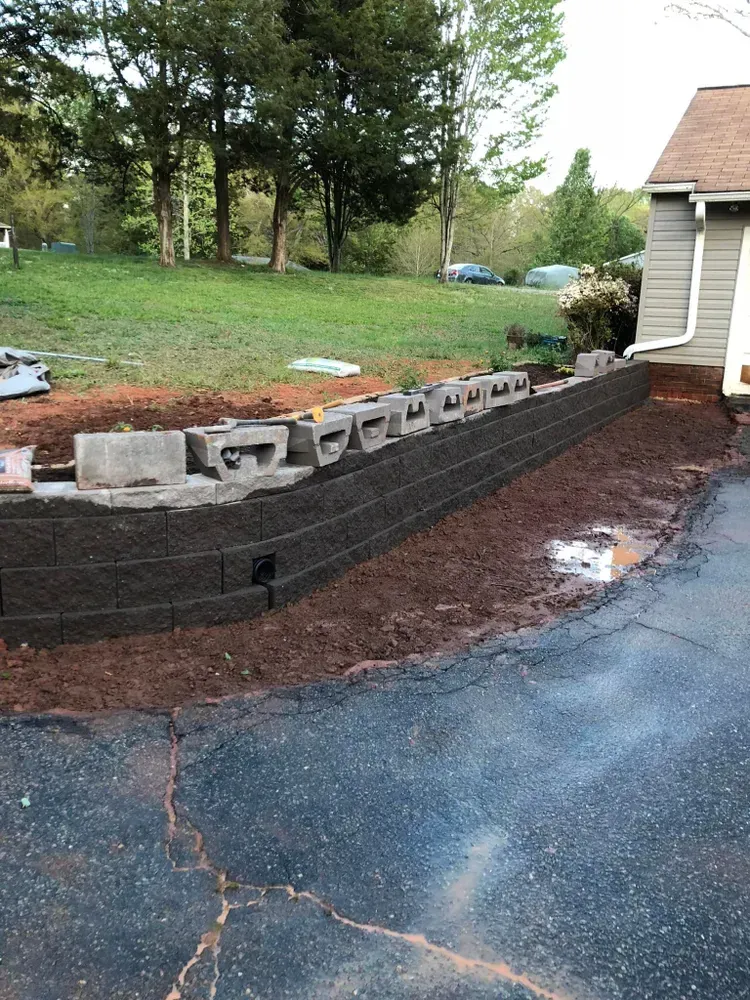 Curved retaining wall blocks along a driveway beside a house, with trees and yard in the background