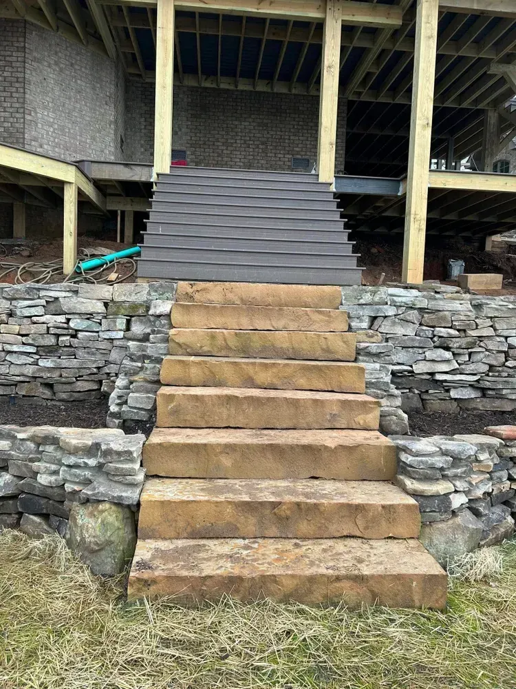 Stone staircase leading to a raised wooden deck under a building, with a stacked-stone retaining wall.