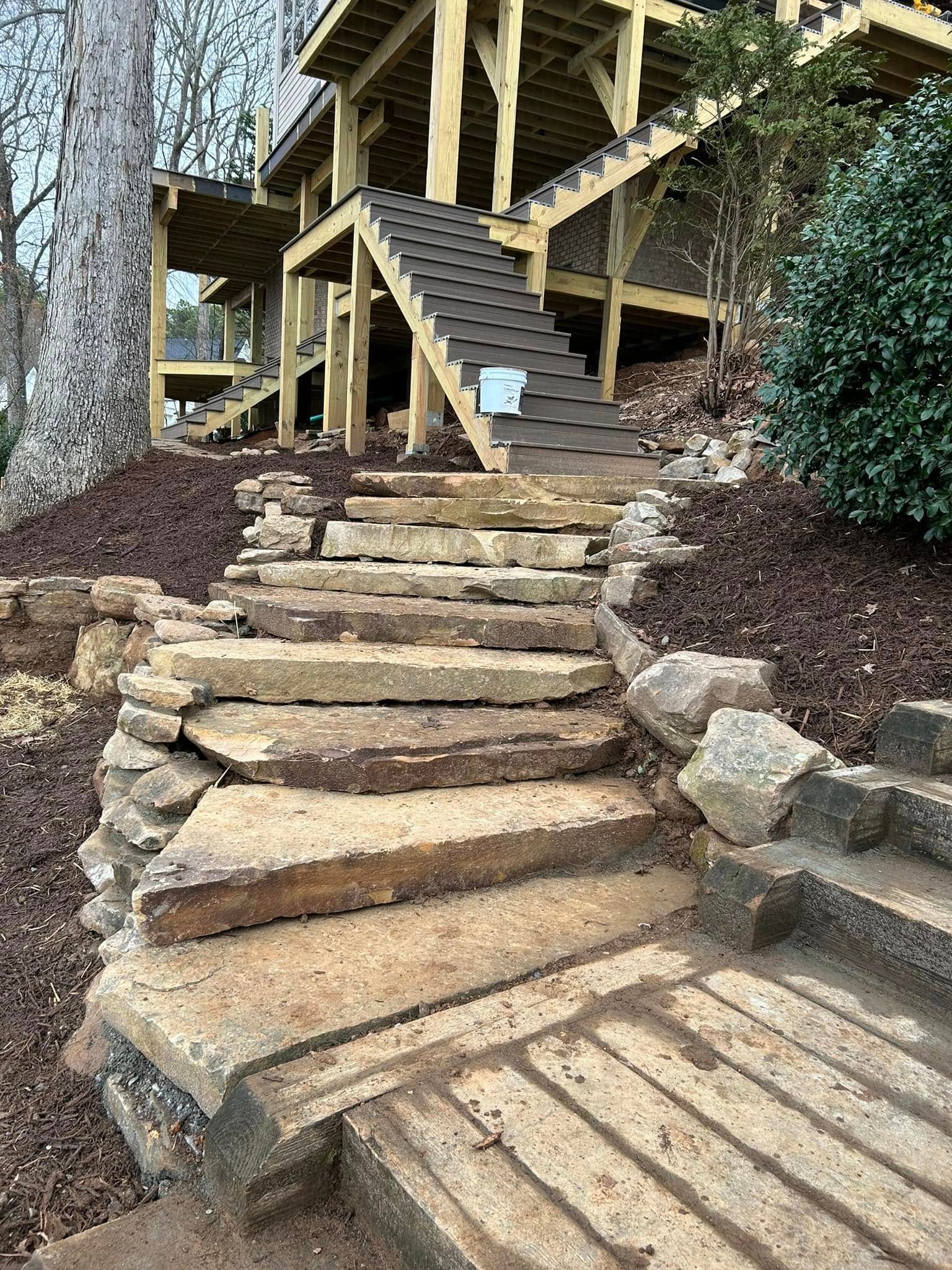 Stone steps climbing a wooded hillside to a raised wooden deck with railings and support posts