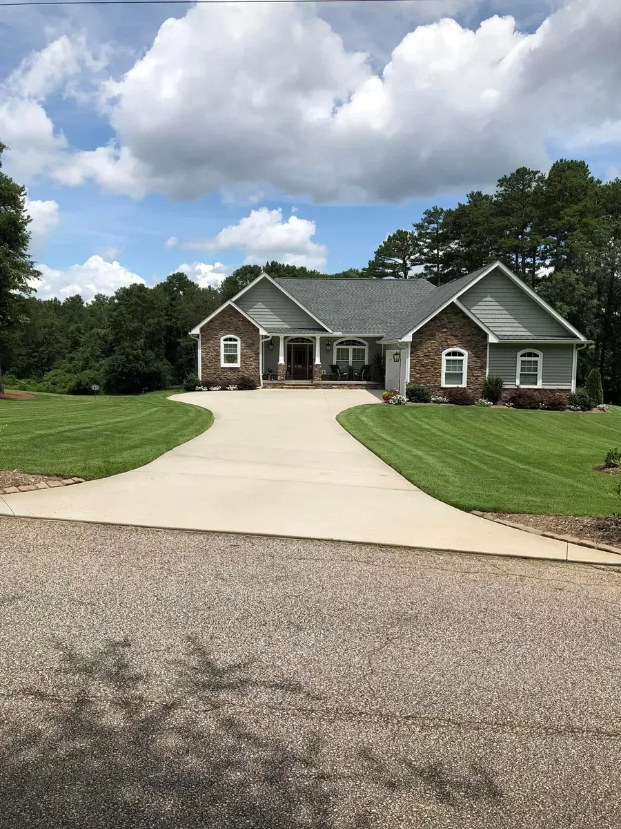 Brick house with a gray roof and curved driveway under a cloudy sky