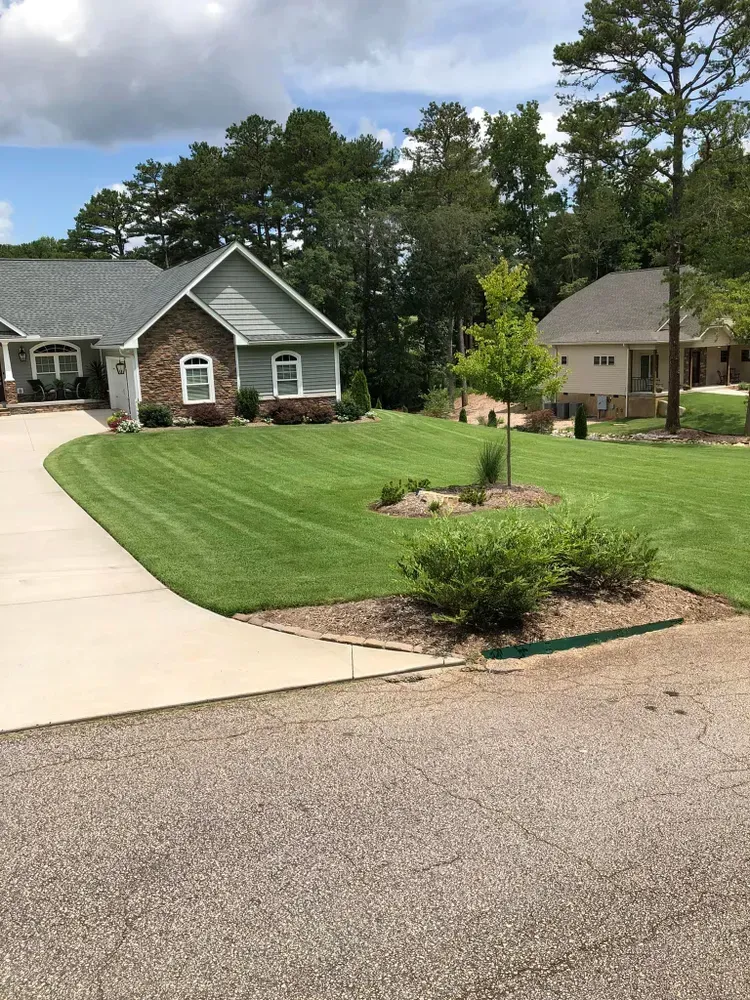 Suburban homes with landscaped lawn, curved driveway, and trees under a partly cloudy sky