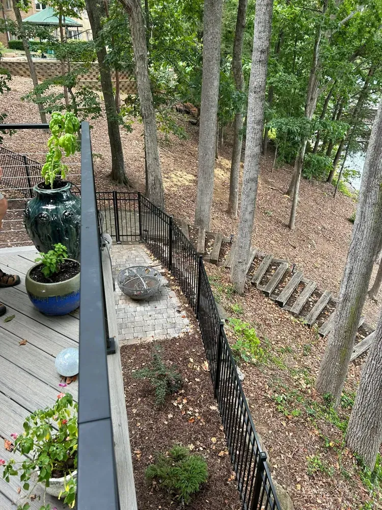 Wooden deck overlooking a wooded hillside with black railings and large potted plants