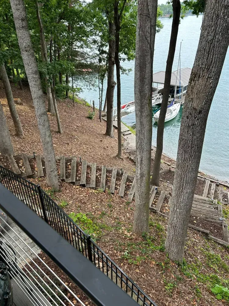 Wooded lakeside view with a docked boat, stone steps, and a railing overlooking the water