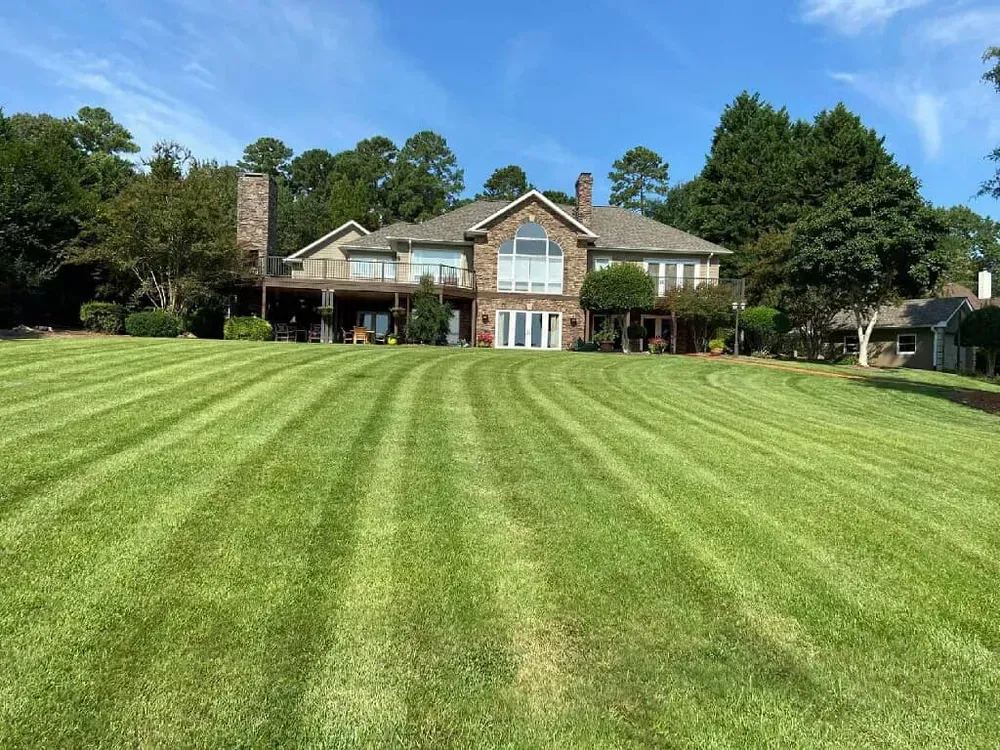Large brick house with a manicured striped lawn under a clear blue sky