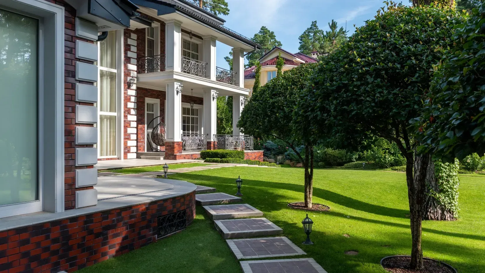 Modern white house with a landscaped lawn, stone path, and trimmed trees in bright sunlight