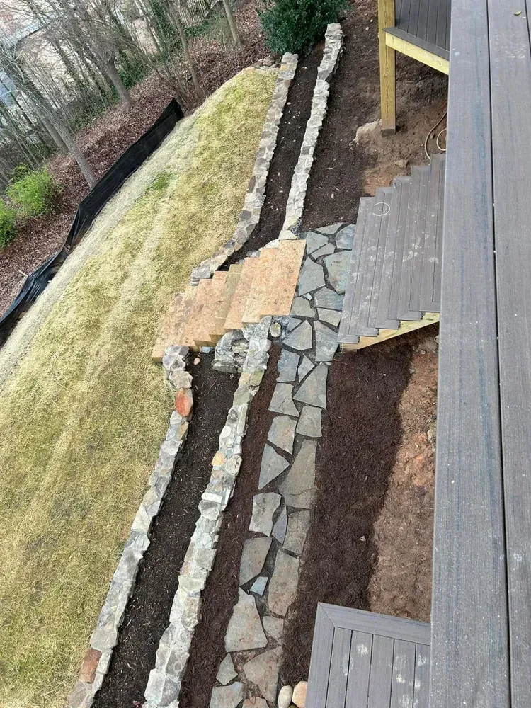 Stone garden path beside a deck, with steps, retaining walls, and sloped grass in a yard.