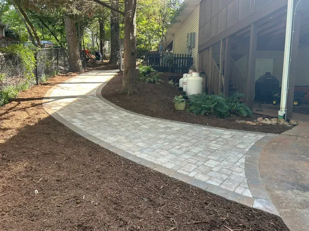 Curved paver walkway through a shaded yard beside a house and trees
