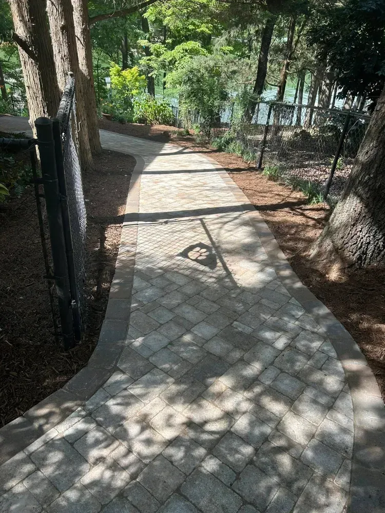 Sunny stone-paved path curving through a wooded area with fence posts on both sides