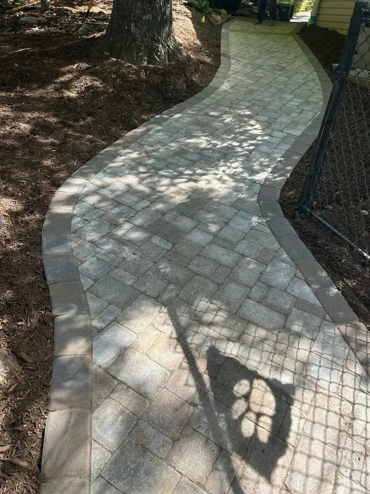 Curved stone walkway beside a fence and trees with dappled sunlight and shadows