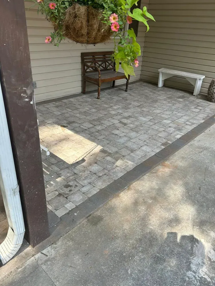 Patio with gray pavers, wooden bench, white bench, hanging flowers, and shaded ground near a doorway