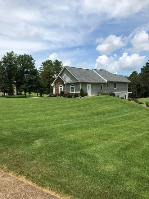 Single-story gray house with white trim on a large green lawn under a partly cloudy sky