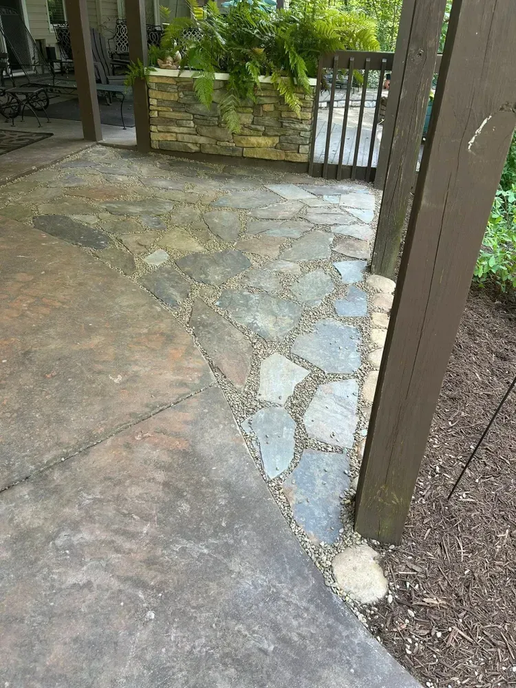 Stone patio with a curved edge, beside a gate and green plants.