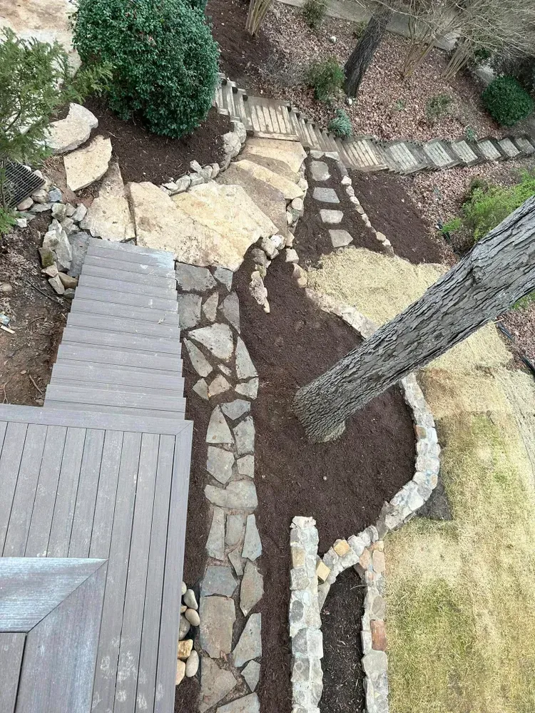 Curved stone garden path beside a deck and tree in a landscaped yard