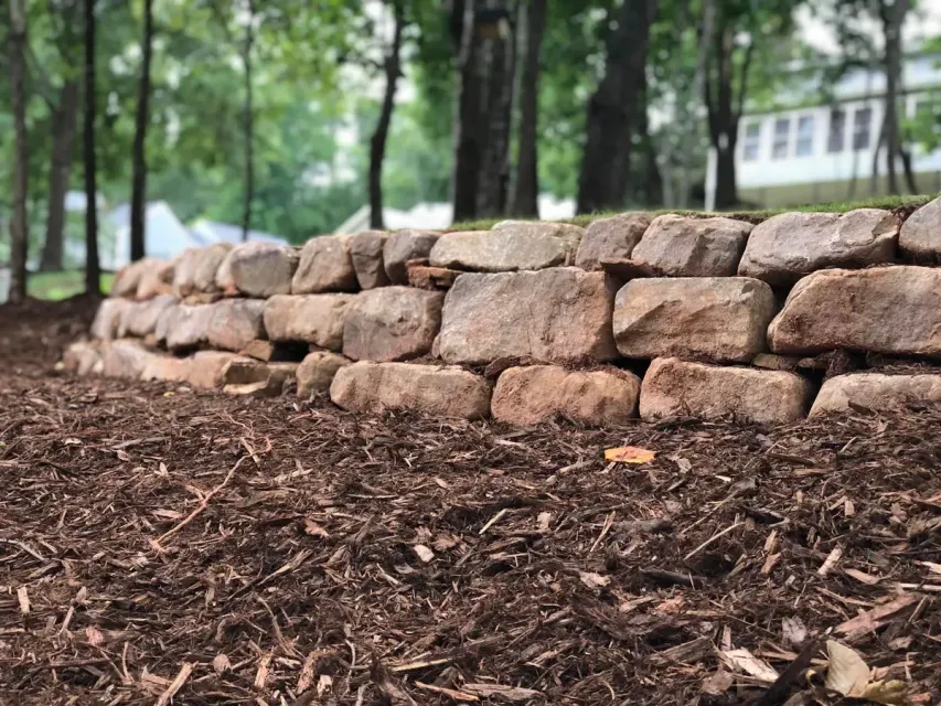 Stone retaining wall in a mulched park area with trees in the background
