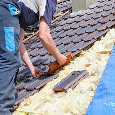 A man is laying tiles on a roof.