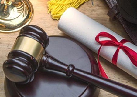 A wooden judge 's gavel is sitting on a wooden table next to a diploma.