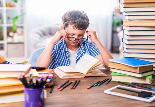 A young boy is sitting at a desk reading a book.