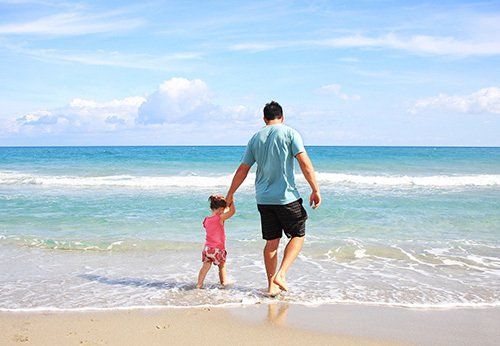 A man and a little girl are walking on the beach holding hands.