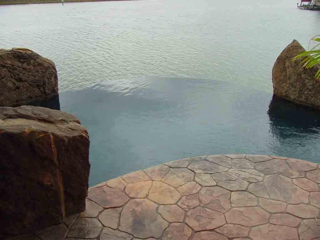 A swimming pool surrounded by rocks next to a body of water.