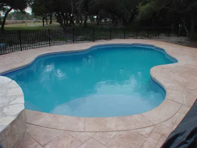 A large swimming pool with a fence around it and trees in the background.