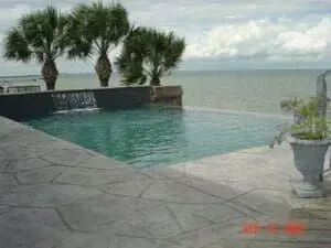 A swimming pool with a waterfall and palm trees overlooking the ocean.
