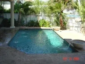 A large swimming pool in the backyard of a house surrounded by palm trees.