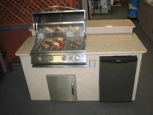 A grill is sitting on top of a counter next to a refrigerator.