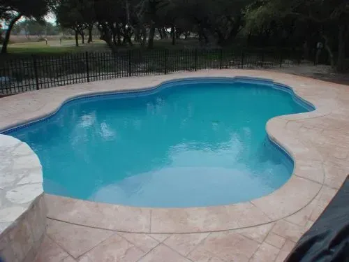 A large swimming pool with a fence around it and trees in the background.