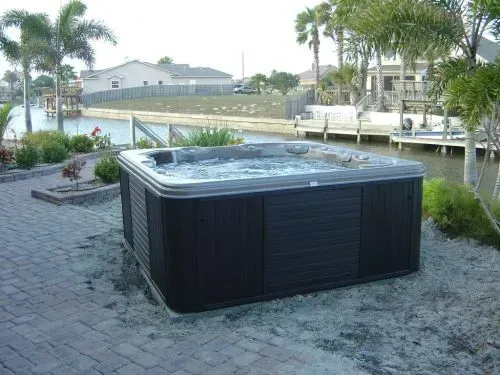 A hot tub is sitting on a brick patio next to a body of water