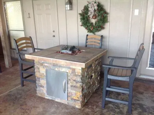 A fire pit table with chairs and a wreath on the wall.