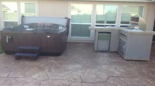 A hot tub is sitting on a patio next to a grill.