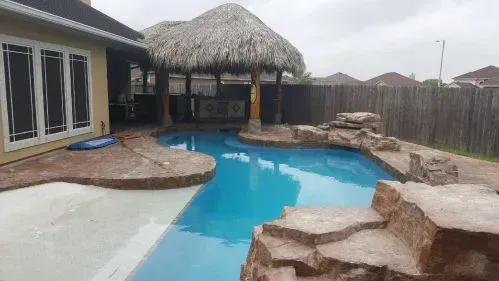 A large swimming pool in the backyard of a house with a thatched roof.