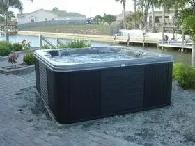 A hot tub is sitting on a brick patio next to a body of water.