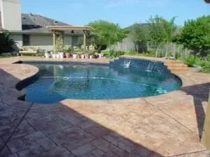 A large swimming pool with a waterfall in the backyard of a house.
