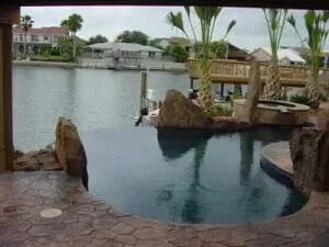 A large swimming pool surrounded by rocks and palm trees next to a body of water.