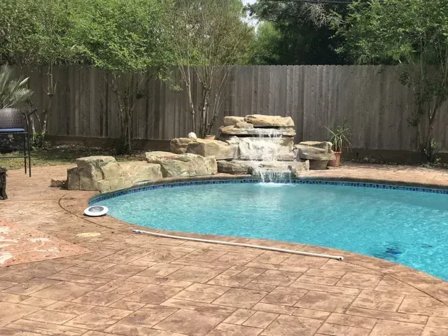 A large swimming pool with a waterfall in the backyard.