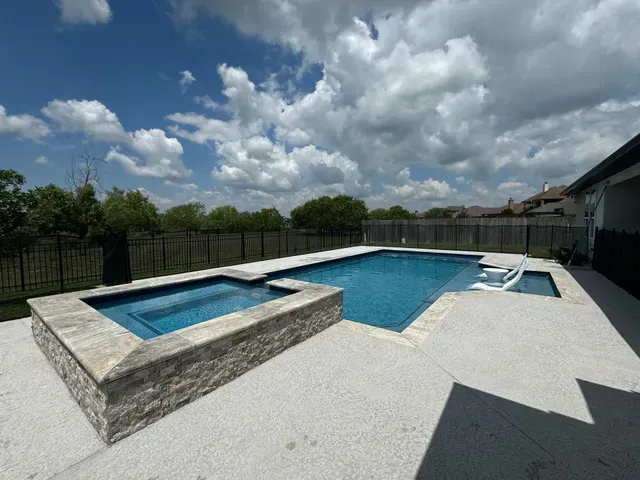 A large swimming pool with a hot tub in the backyard of a house.