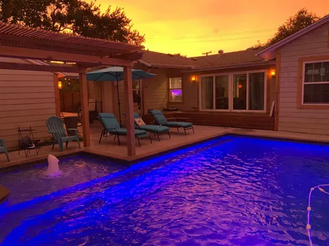 A large swimming pool is lit up with blue lights in front of a house.