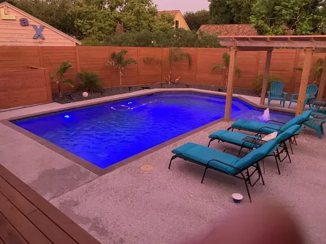 A large swimming pool surrounded by chairs and a pergola