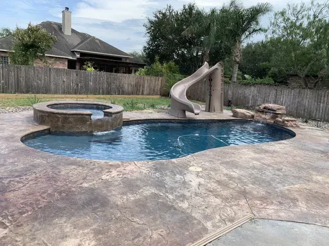 A swimming pool with a slide and a hot tub in the backyard of a house.