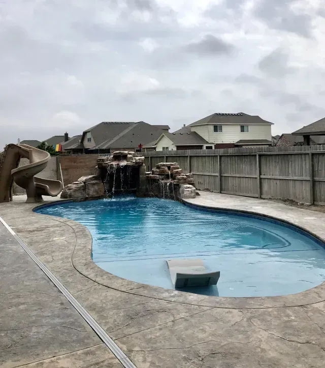 A large swimming pool with a waterfall and a slide in a backyard.