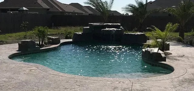 A large swimming pool with a waterfall in the backyard of a house.