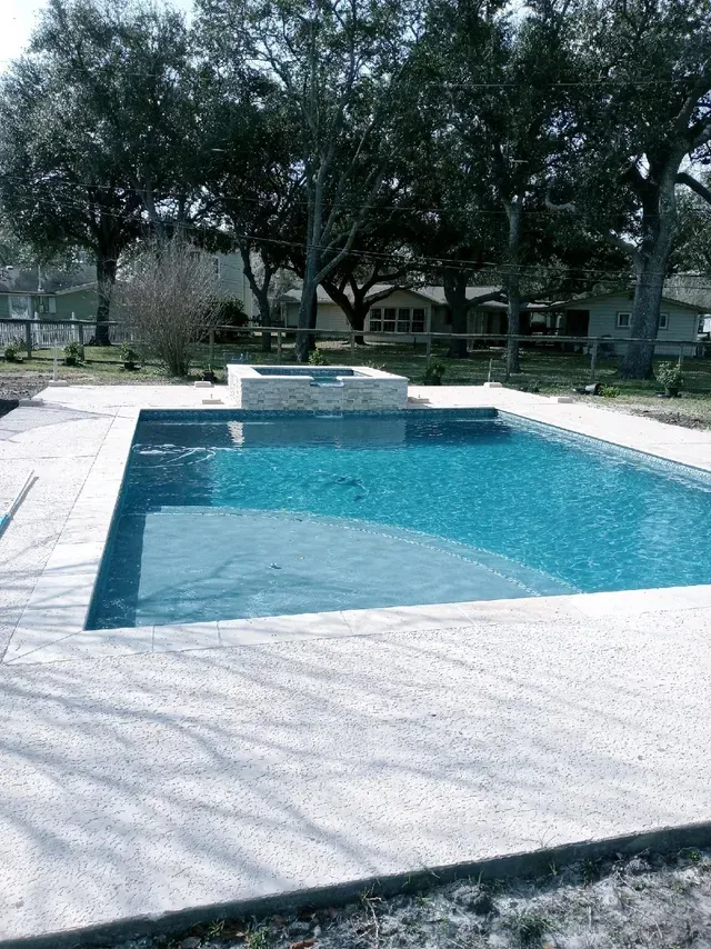A large swimming pool is surrounded by trees in a backyard.