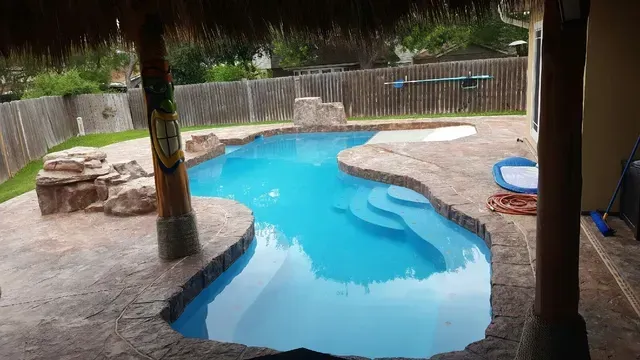 A large swimming pool in the backyard of a house with a thatched roof.