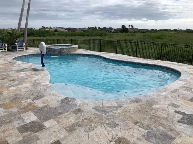 A large swimming pool surrounded by a tiled patio and a fence.