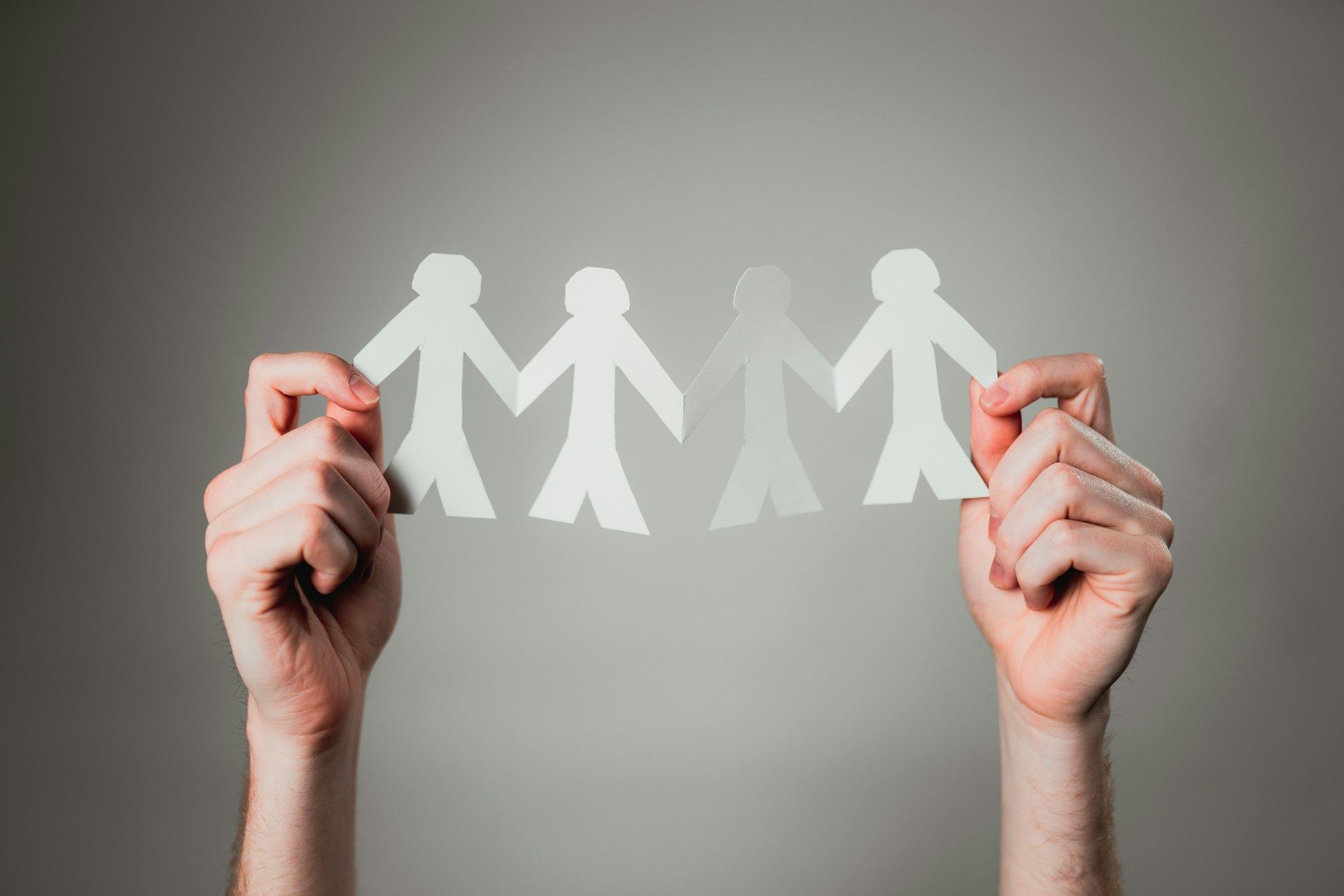 Hands holding a paper chain of people silhouettes, symbolizing unity.