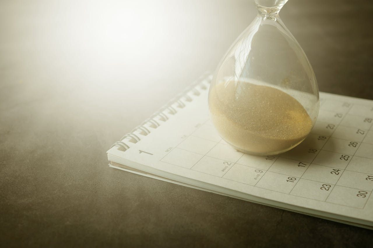 A sand glass timer sitting on top of a calendar on a desk