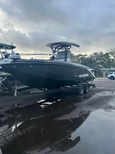 A black boat on a trailer sits on wet pavement under a cloudy sky.