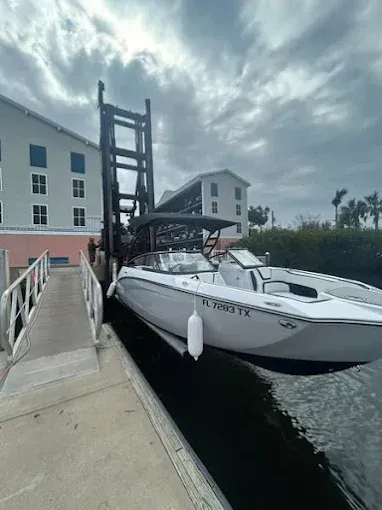 Boat being lifted by a boat lift at a dock, in front of buildings, under a cloudy sky.