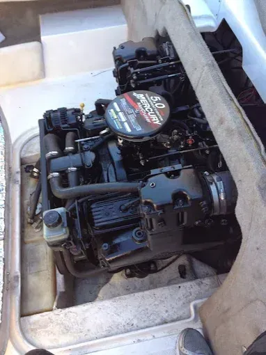 Mercury 5.0 boat engine, black with a red and black air filter, installed inside of a white boat.